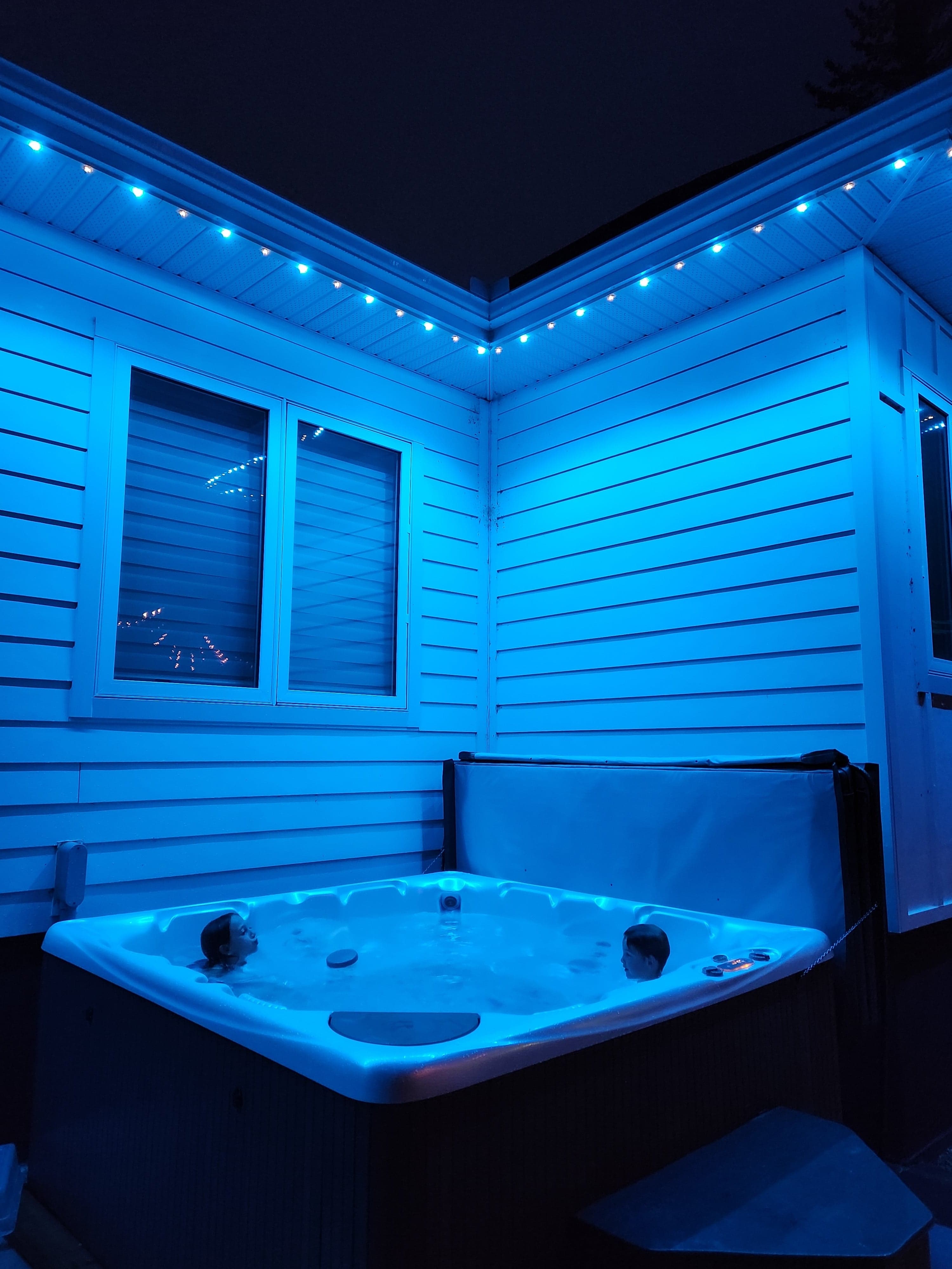 Teal permanent LED soffit lighting in a backyard hot tub area at night