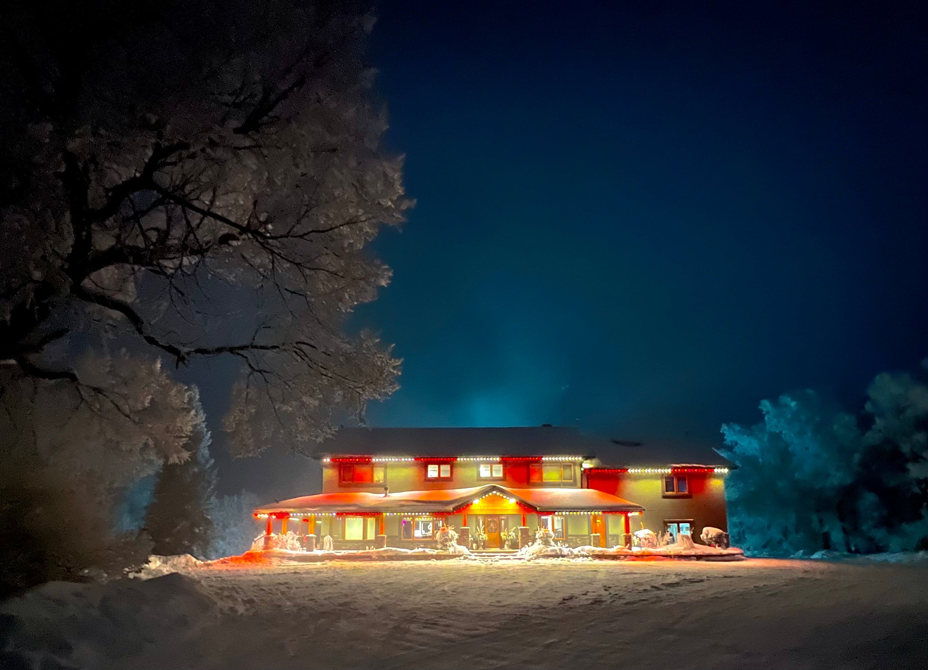 Winter night view of a home with red permanent LED roofline lighting and lit Christmas trees, snow on the ground